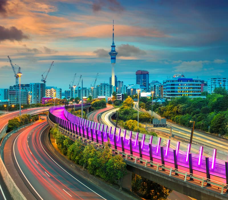 A curving road with blurred car lights and Auckland buildings and Skytower in the background Credit: Auckland Skyline